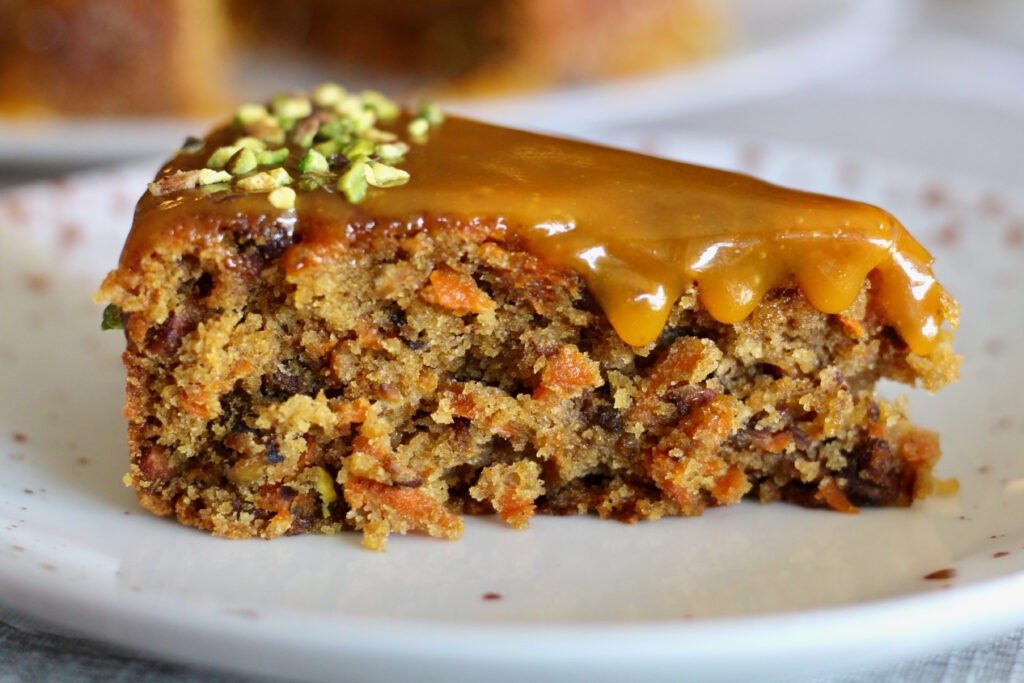 Slice of pistachio, orange and cardamom carrot cake with caramel glaze